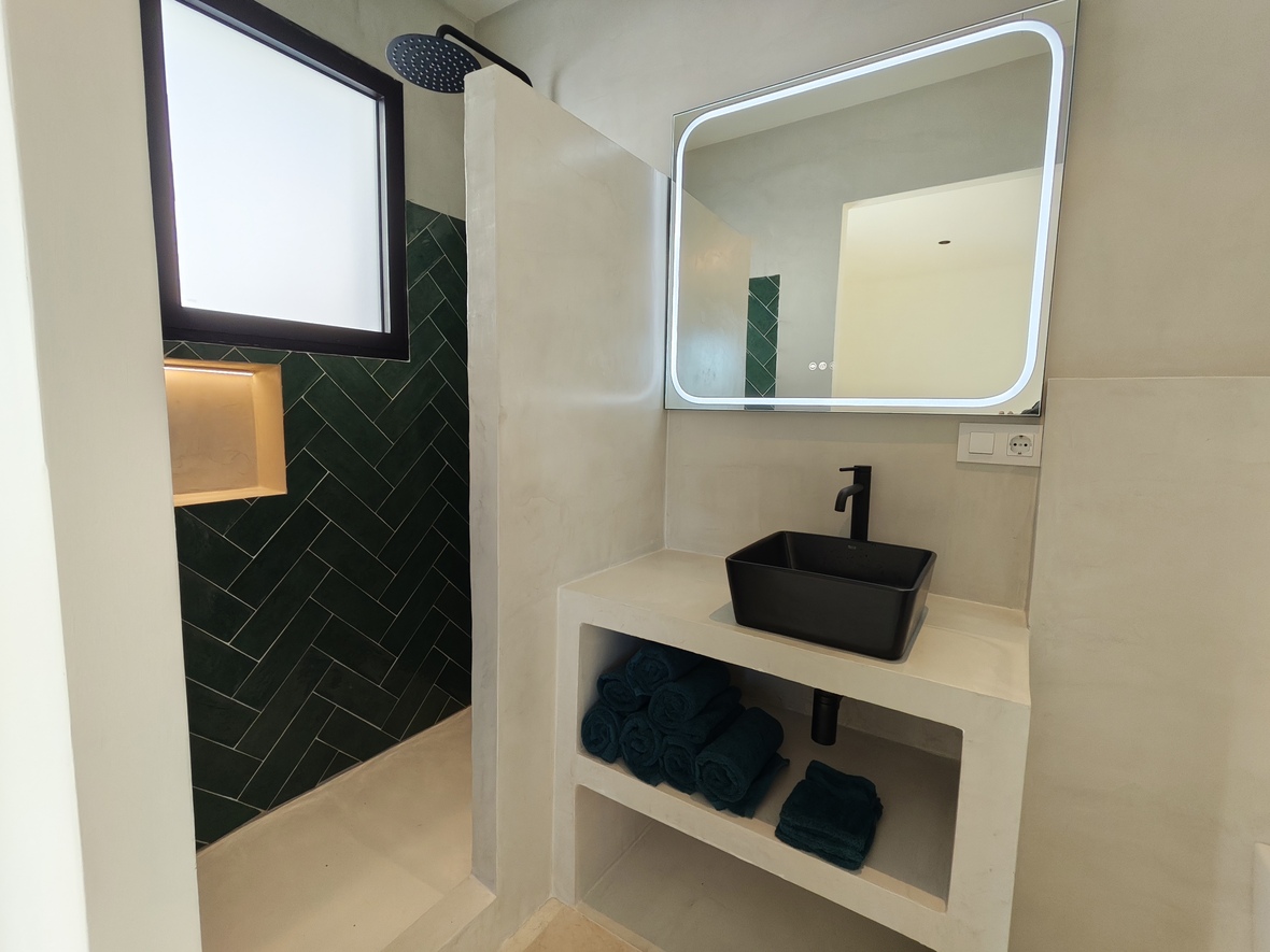 Moderne badkamer met een zwarte opzetwastafel op een microcement meubel, een verlichte LED-spiegel en een inloopdouche met groene visgraattegels.