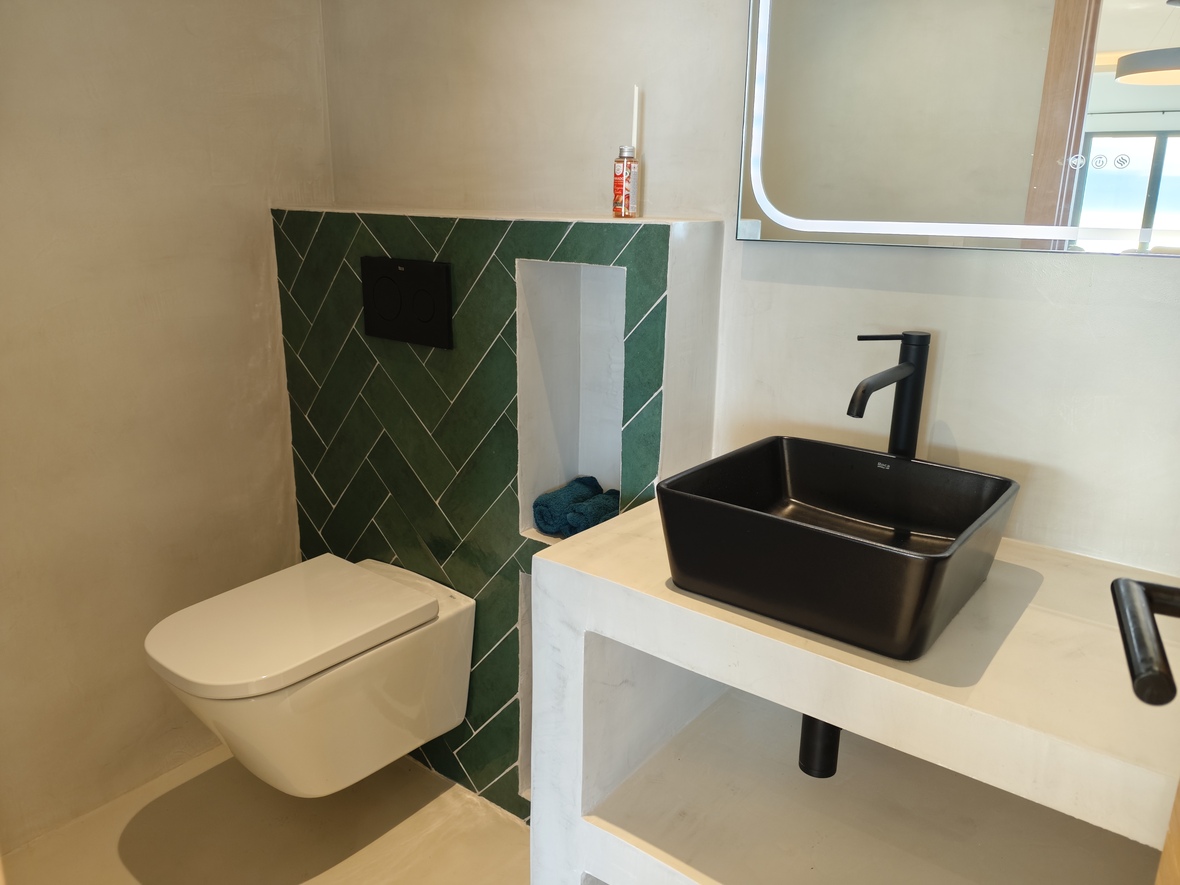 Moderne badkamer met een zwarte opzetwastafel op een microcement meubel, groene visgraat tegels en een wandcloset.