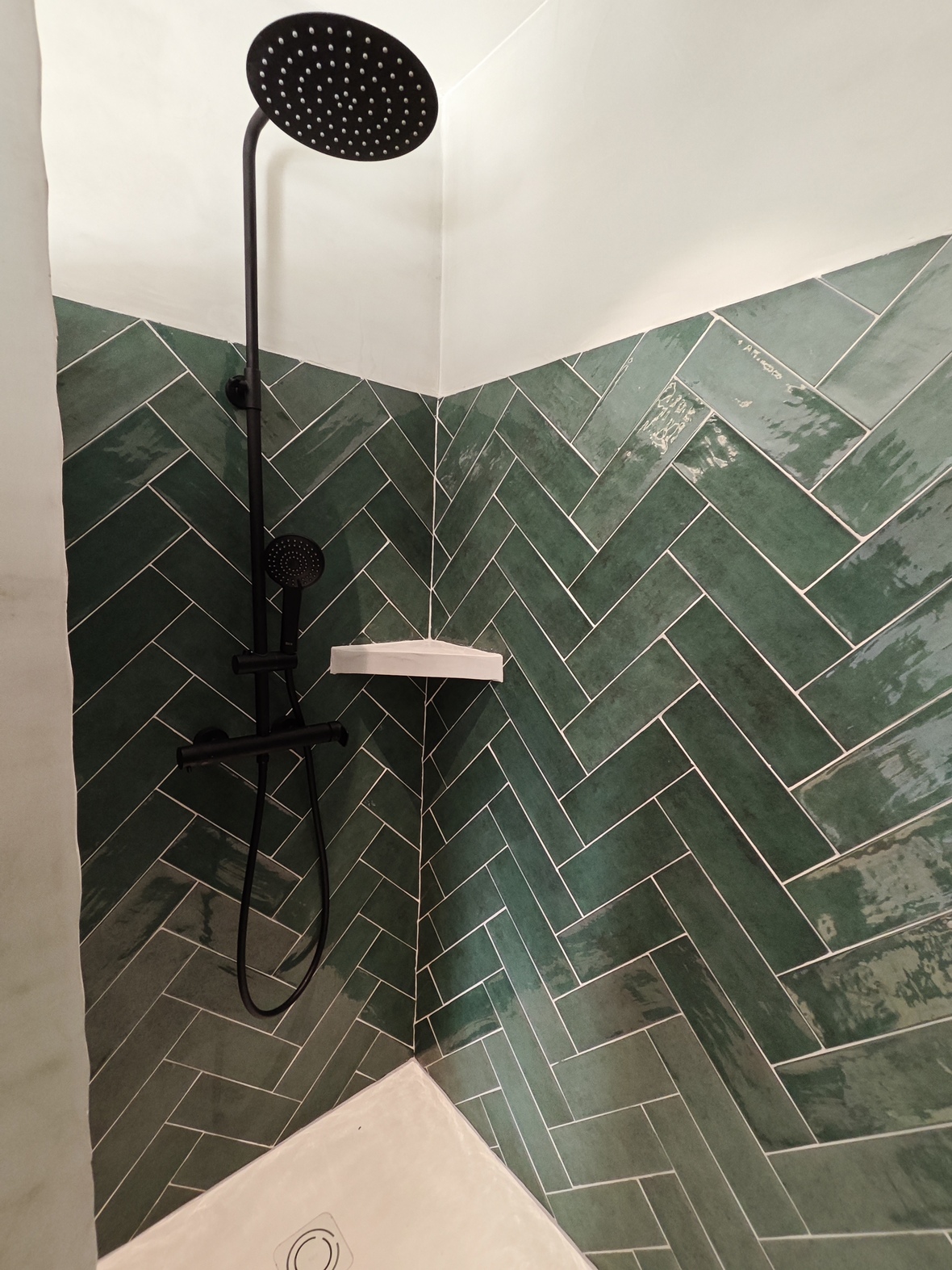 Moderne douche met smaragdgroene tegels in visgraatmotief, uitgerust met matzwarte kranen en een grote regendouchekop.