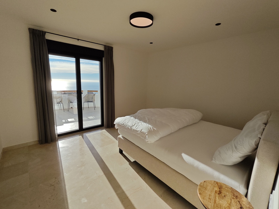 Moderne slaapkamer met gepolijste marmeren vloer, tweepersoonsbed en glazen schuifdeuren naar een terras met weids uitzicht op zee.