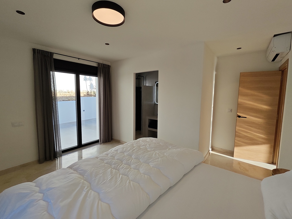Moderne slaapkamer met gepolijste natuurstenen vloer, directe toegang tot het terras en een aangrenzende badkamer met strakke afwerking.