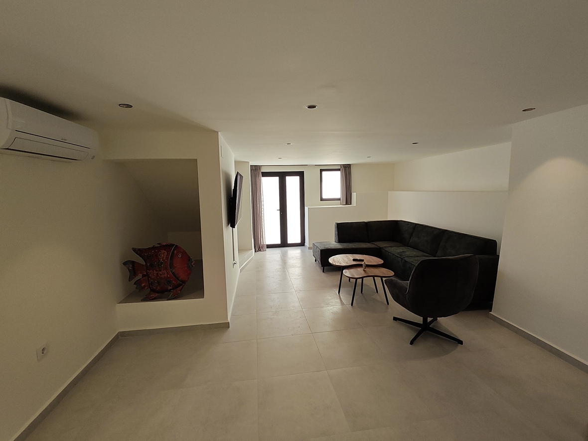 Moderne woonkamer met een donkergrijze hoekbank, houten tafels en een decoratieve nis. Voorzien van airconditioning, inbouwspots en een lichte tegelvloer.