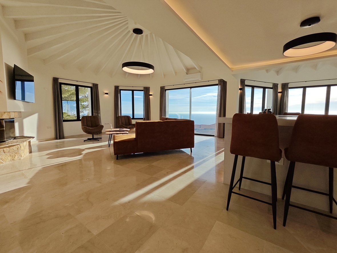 Open woonruimte met een radiaal balkenplafond, gepolijste marmeren vloeren en panoramisch zeezicht. Voorzien van een stenen open haard en moderne cirkelvormige verlichting.