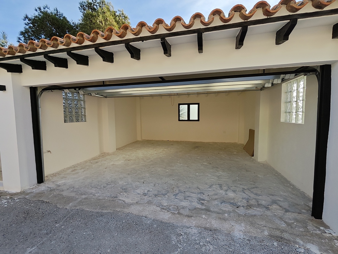 Ruime garage met betonnen vloer, glasblokken voor natuurlijk licht en een traditioneel pannendak met donkere houten balken.
