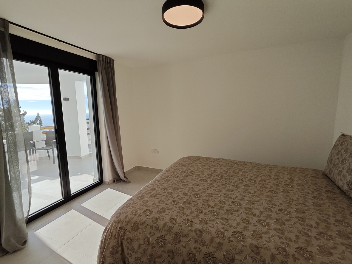 Slaapkamer met tweepersoonsbed, bloemendessin en directe toegang tot een privéterras met uitzicht op zee via glazen schuifdeuren.