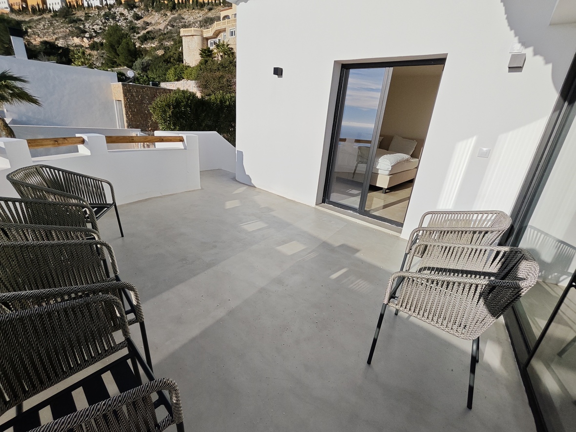 Terras met een gladde betonvloer en moderne gevlochten stoelen, met directe toegang tot de slaapkamer via een glazen schuifdeur.