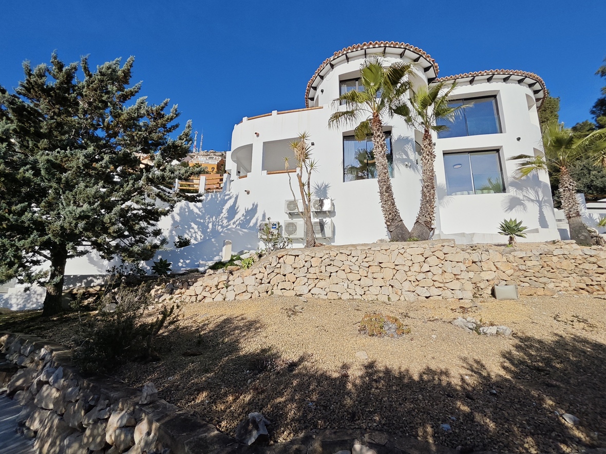 Witte mediterrane villa met ronde architectuur, natuurstenen muren en een terrasvormige tuin voorzien van palmbomen en grind.