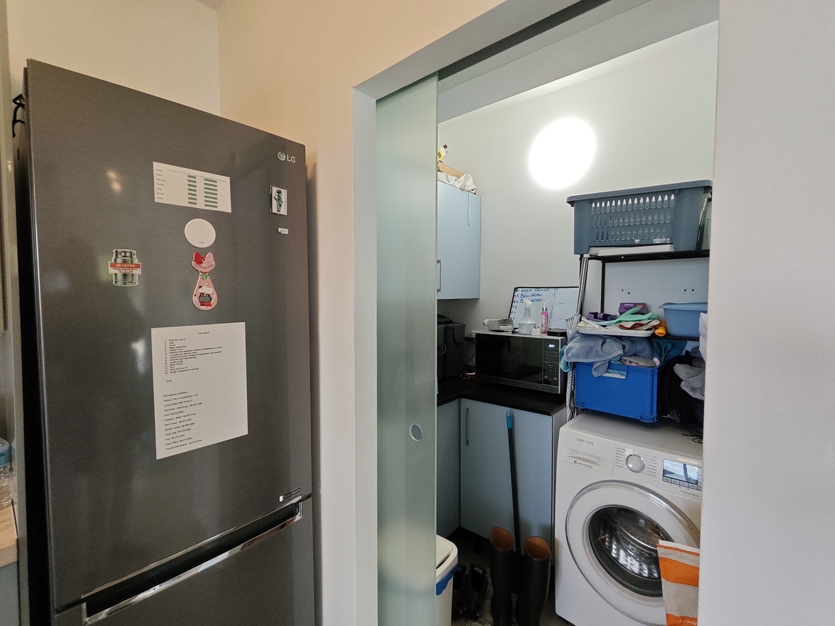Bijkeuken met een matglazen schuifdeur, voorzien van een Samsung wasmachine, magnetron en lichtblauwe kasten naast een grote LG koelkast.