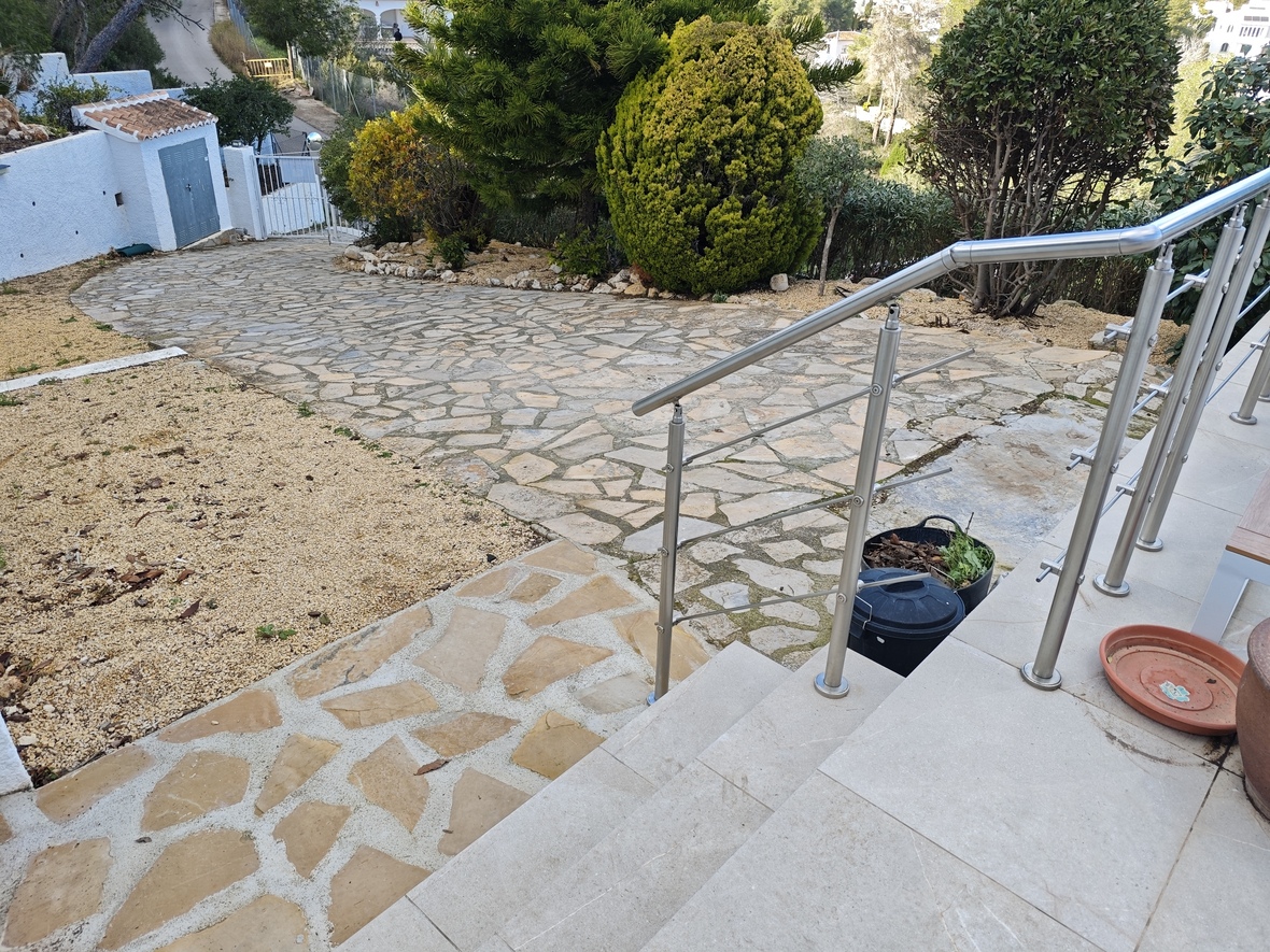 Buitenaanzicht met een oprit van natuursteen omgeven door mediterrane beplanting en een trap met roestvrijstalen leuning.