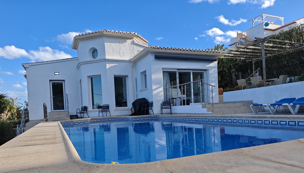 Buitenaanzicht van een witte mediterrane villa met privézwembad, zonneterras met blauwe ligstoelen en een houten pergola.