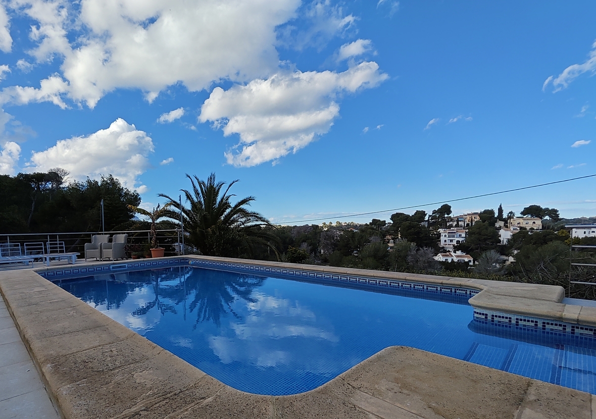 Buitenzwembad met blauwe mozaïektegels en stenen rand, met uitzicht op het omliggende mediterrane woonlandschap en de lokale vegetatie.