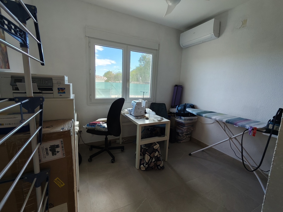 Functionele hobbykamer of kantoor met naaihoek, strijkplank en airconditioning. De ruimte is voorzien van een tegelvloer en natuurlijke lichtinval via het dubbele raam.