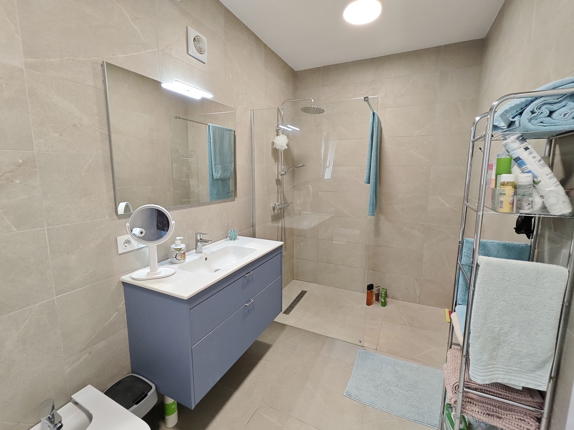 Moderne badkamer met blauw zwevend wastafelmeubel, inloopdouche met glazen wand en zandkleurige keramische betegeling.