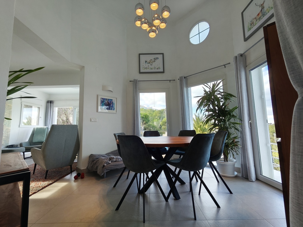 Moderne eethoek met een ronde houten tafel, donkere kuipstoelen en hoge plafonds met een rond accentvenster en een chromen hanglamp.