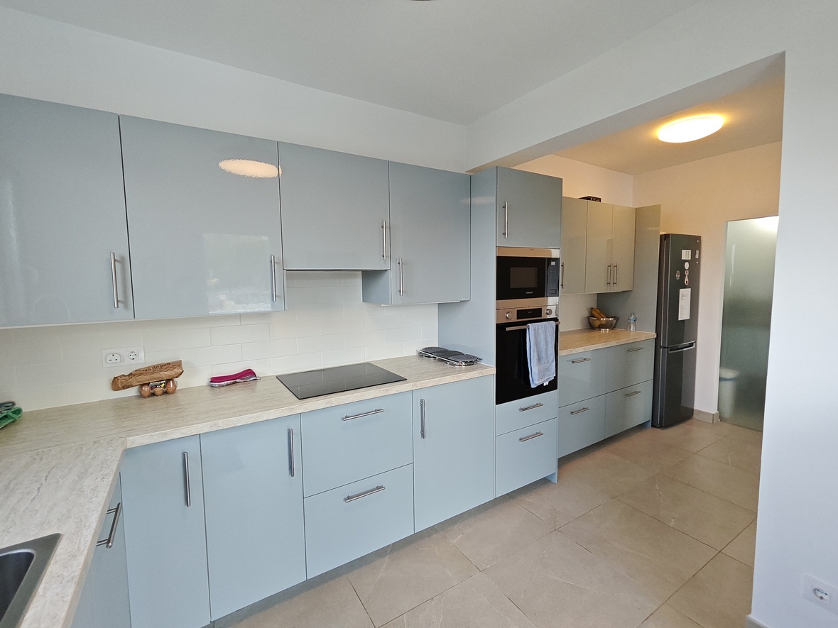 Moderne keuken met lichtblauwe hoogglans kasten, een werkblad met steeneffect en inbouwapparatuur op een vloer van grote beige tegels.