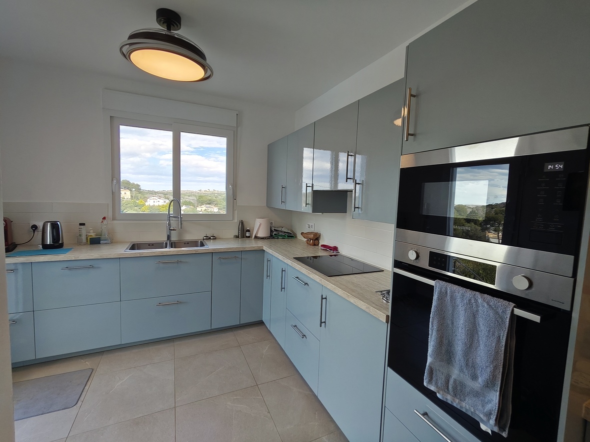 Moderne keuken met lichtblauwe kasten, werkblad met houtlook en geïntegreerde Samsung-apparatuur. Een groot raam biedt uitzicht op het omliggende landschap.