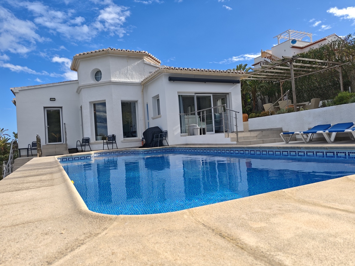Privézwembad met blauwe mozaïektegels, omgeven door een stenen terras en een witgekalkte villa met een kenmerkend cirkelvormig torenelement.