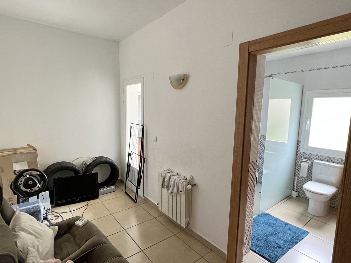 Functionele ruimte met tegelvloer en radiator, verbonden met een badkamer voorzien van een inloopdouche met glazen wand en natuurlijke ventilatie.
