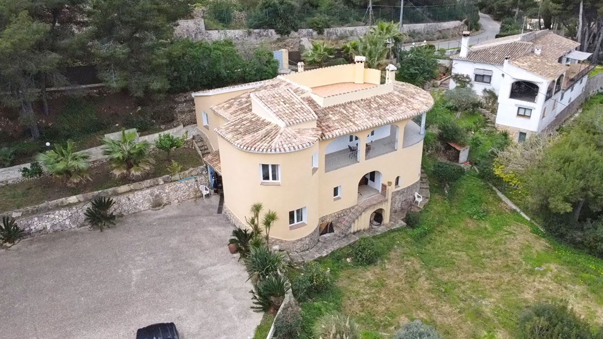 Luchtfoto van de mediterrane villa met een gebogen gevel, terracotta pannendak en een ruime verharde oprit omgeven door een natuurlijke tuin.