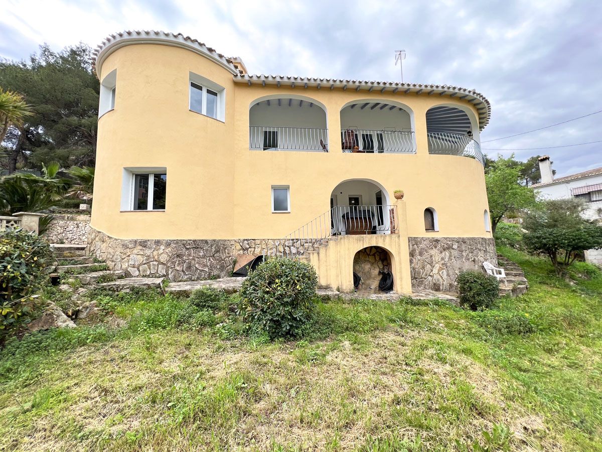 Mediterrane villa met gebogen gele gevel, natuurstenen plint, overdekte terrassen met bogen op de bovenverdieping en een glooiende tuin met stenen trappen.