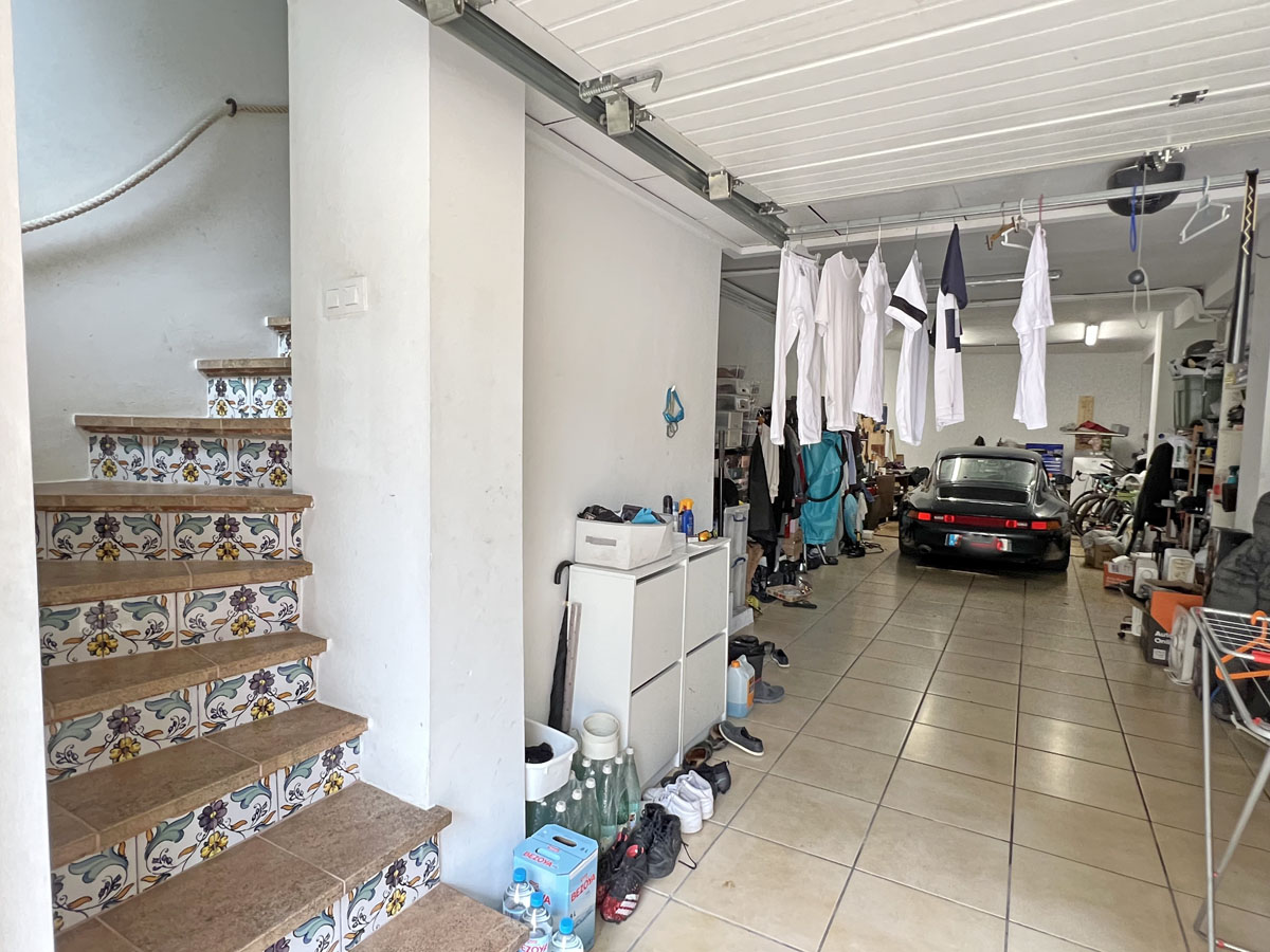 Ruime garage met tegelvloer en bergruimte, voorzien van een interne trap met traditionele mediterrane tegels die toegang biedt tot de woning.