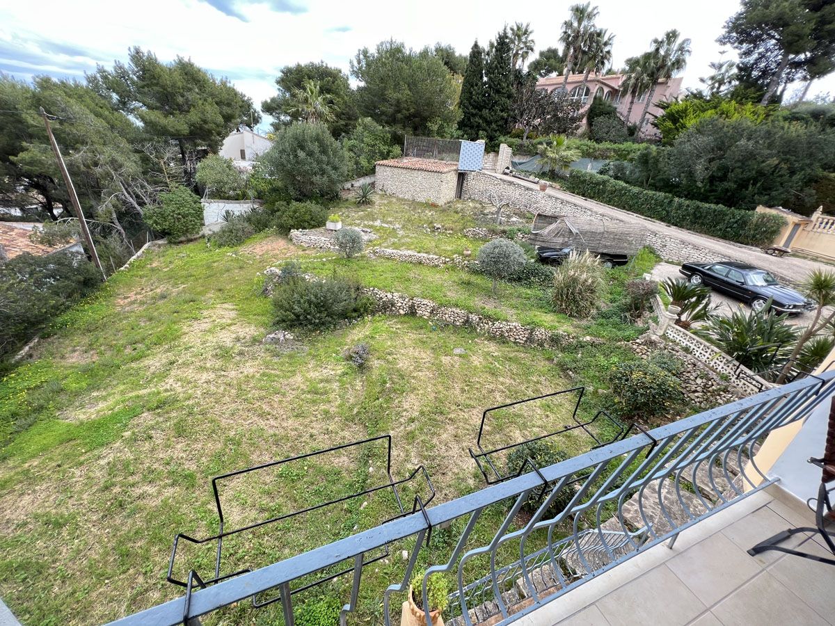 Verhoogd uitzicht vanaf het terras op het terrasvormige perceel met natuurstenen muren en volwassen mediterrane beplanting.