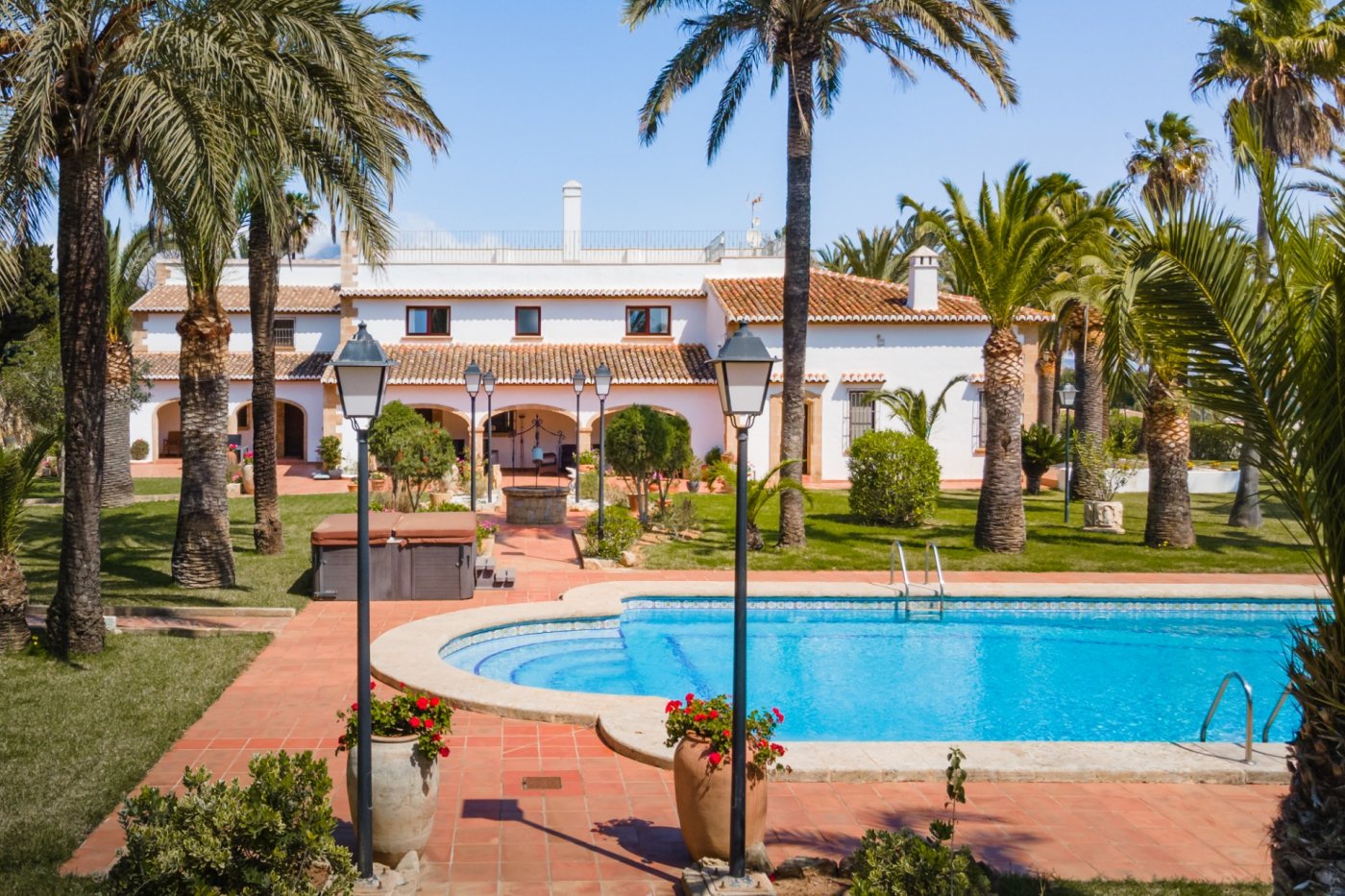 Buitenaanzicht van de mediterrane villa met zwembad, aangelegde tuin met palmbomen en een ruim terracotta terras voorzien van klassieke lantaarnpalen.