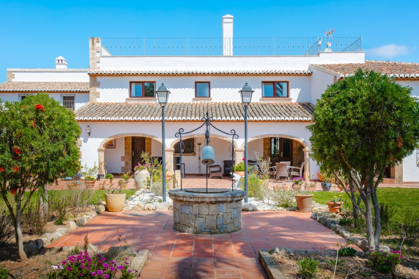 Buitenplaats met een traditionele stenen waterput, terracotta tegels en een witte gevel met bogen van Tosca-natuursteen en mediterrane dakpannen.