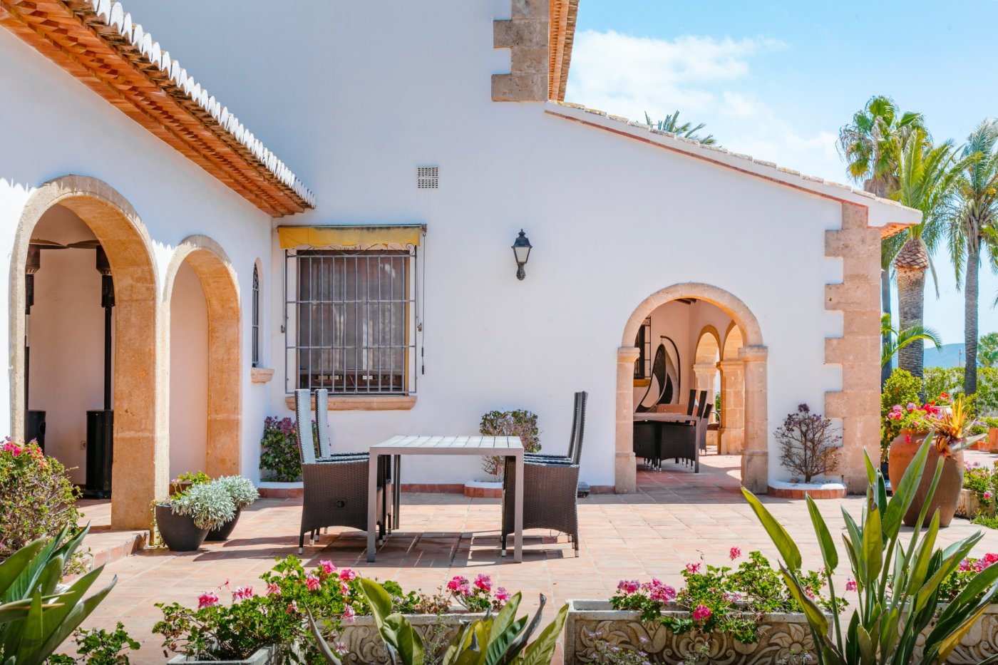 Buitenterras met traditionele Tosca-stenen bogen, terracotta vloertegels en een eethoek in de open lucht, omgeven door mediterrane bloembakken.