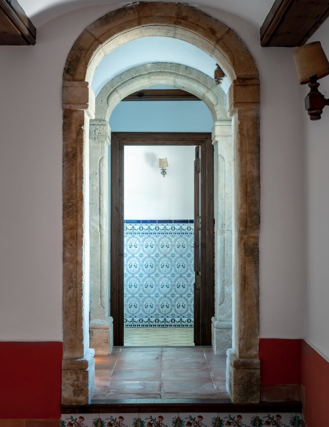 Gang met traditionele Tosca-stenen bogen die leiden naar een kamer met decoratieve wandtegels en terracotta vloeren.