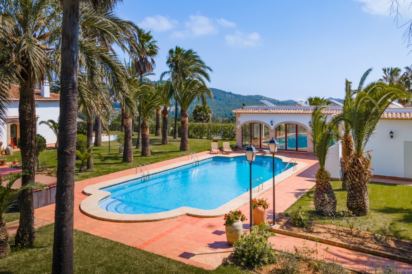 Groot zwembad van 16x7m met terracotta terras, omgeven door een uitgestrekte palmentuin en een gastenverblijf met traditionele mediterrane bogen.
