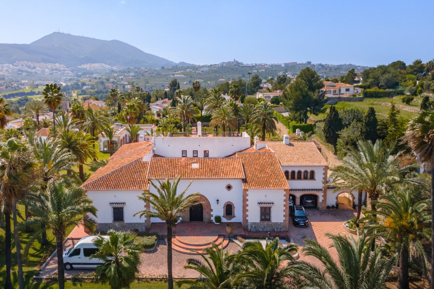 Luchtfoto van de mediterrane villa met terracotta pannendaken, Tosca-stenen bogen en een uitgestrekt perceel met palmbomen en panoramisch uitzicht op de vallei.