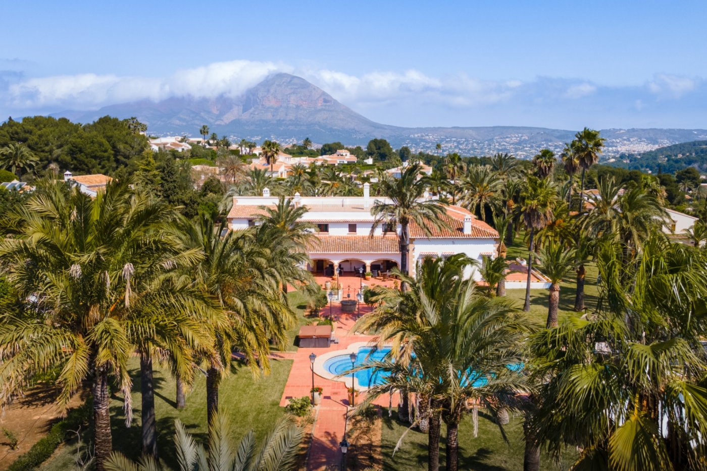 Luchtfoto van de mediterrane villa omgeven door palmbomen, met een groot zwembad en panoramisch uitzicht op de berg Montgó.