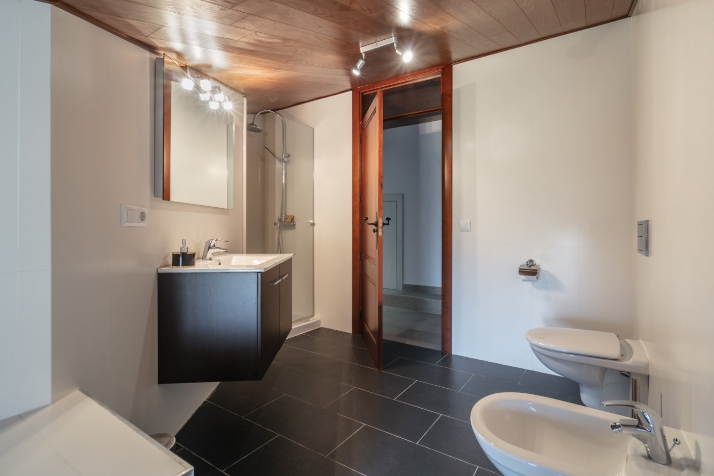 Moderne badkamer met een houten plafond, donkere vloertegels, een zwevend wastafelmeubel en een glazen douchecabine met chromen kranen.