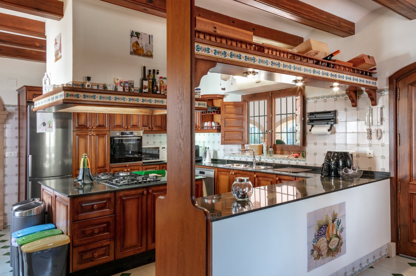 Rustieke keuken met houten balken, donkere granieten werkbladen en traditionele tegels. Voorzien van een kookeiland met gaskookplaat en houten inbouwkasten.