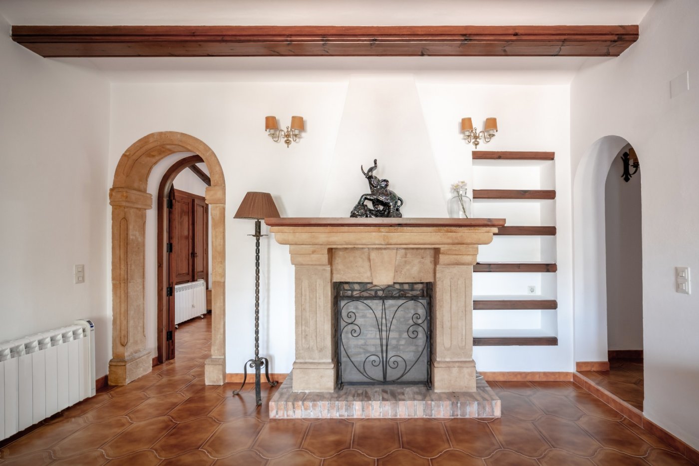 Woonkamer met een open haard van Tosca-steen, terracotta vloertegels en houten balken. Voorzien van een natuurstenen boog en ingebouwde wandplanken.