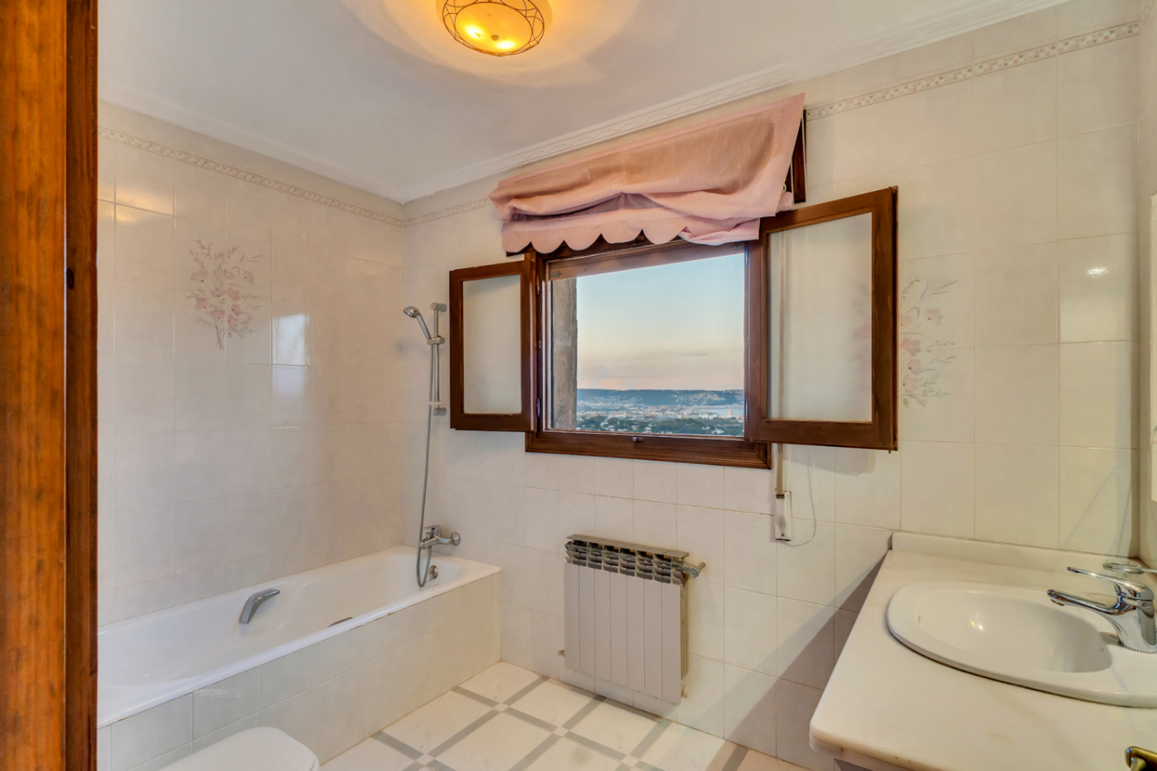 Badkamer met ligbad, tegels met bloemenmotief en een houten raam met panoramisch uitzicht op de zee en de baai van Jávea.