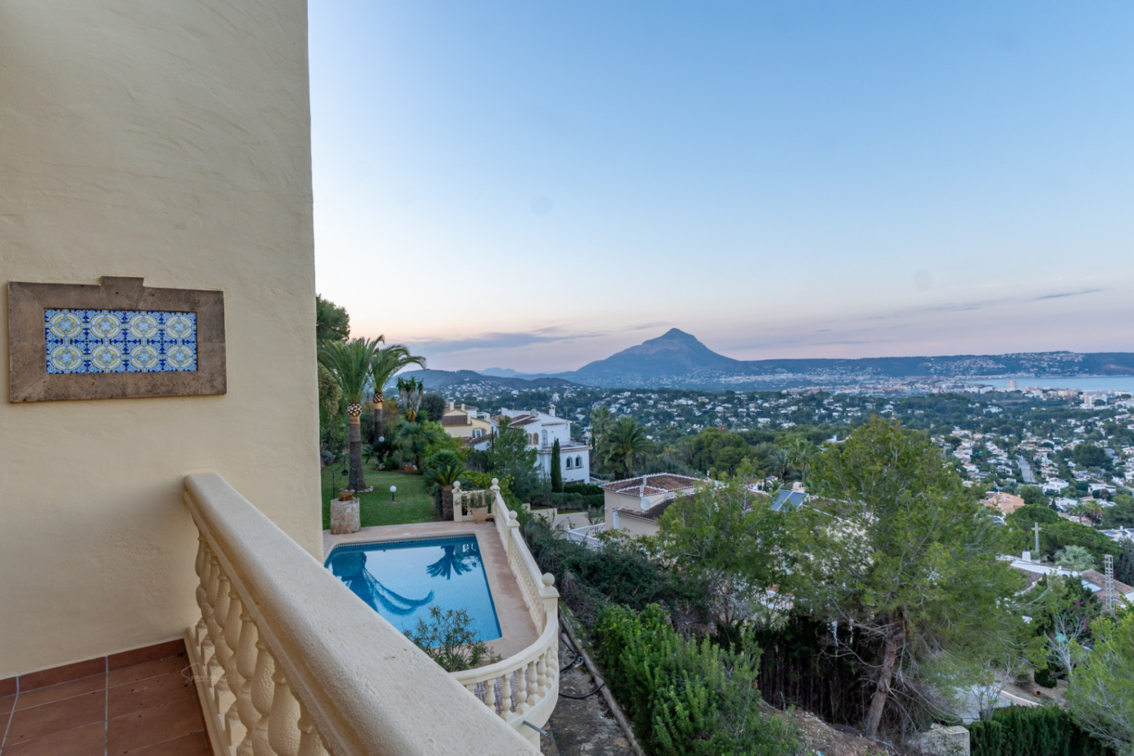 Boventerras met stenen balustrade en decoratief tegelwerk, uitkijkend over het privézwembad, de mediterrane tuin en panoramisch uitzicht op de Montgó en de baai van Jávea.
