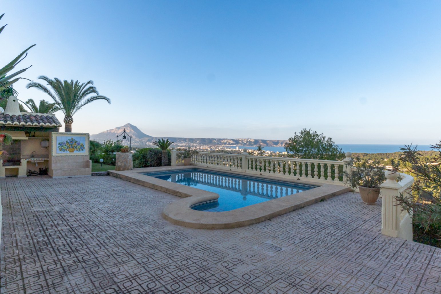 Buitenzwembad op een ruim betegeld terras met balustrades, met panoramisch uitzicht op de Montgó en de baai van Jávea, inclusief een barbecueplek.