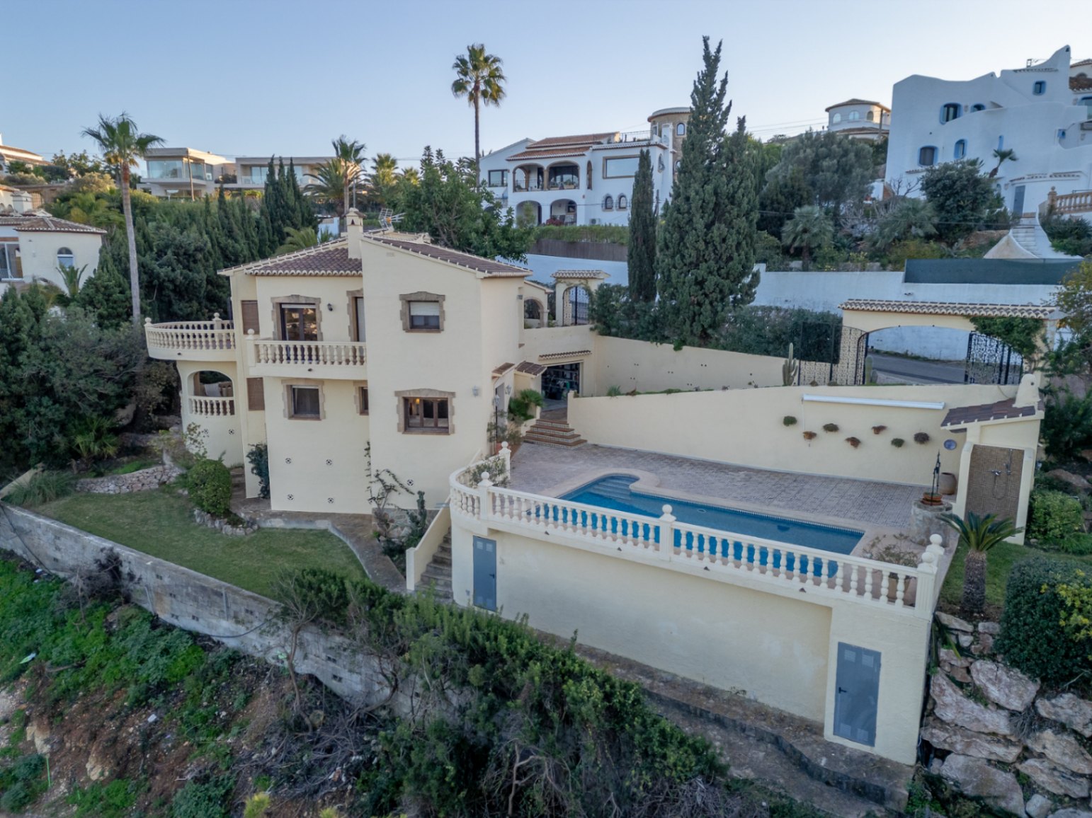 Exterieur van de mediterrane villa met privézwembad, terrassen met witte balustrades en een crèmekleurige gevel met natuurstenen details.