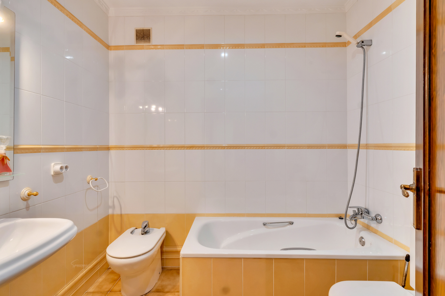 Functionele badkamer voorzien van een ingebouwd ligbad, bidet en witte wandtegels met gele sierlijsten en chromen kranen.