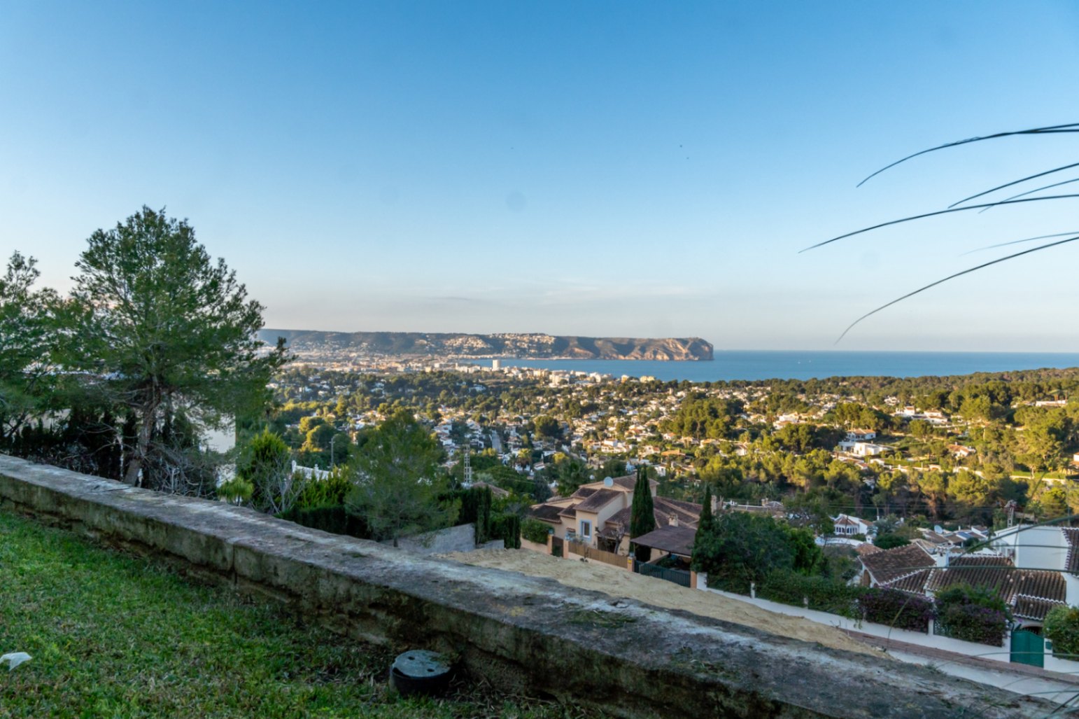 Panoramisch uitzicht vanaf het perceel over de baai van Jávea en Cabo San Antonio, omgeven door mediterrane vegetatie en pijnbomen.