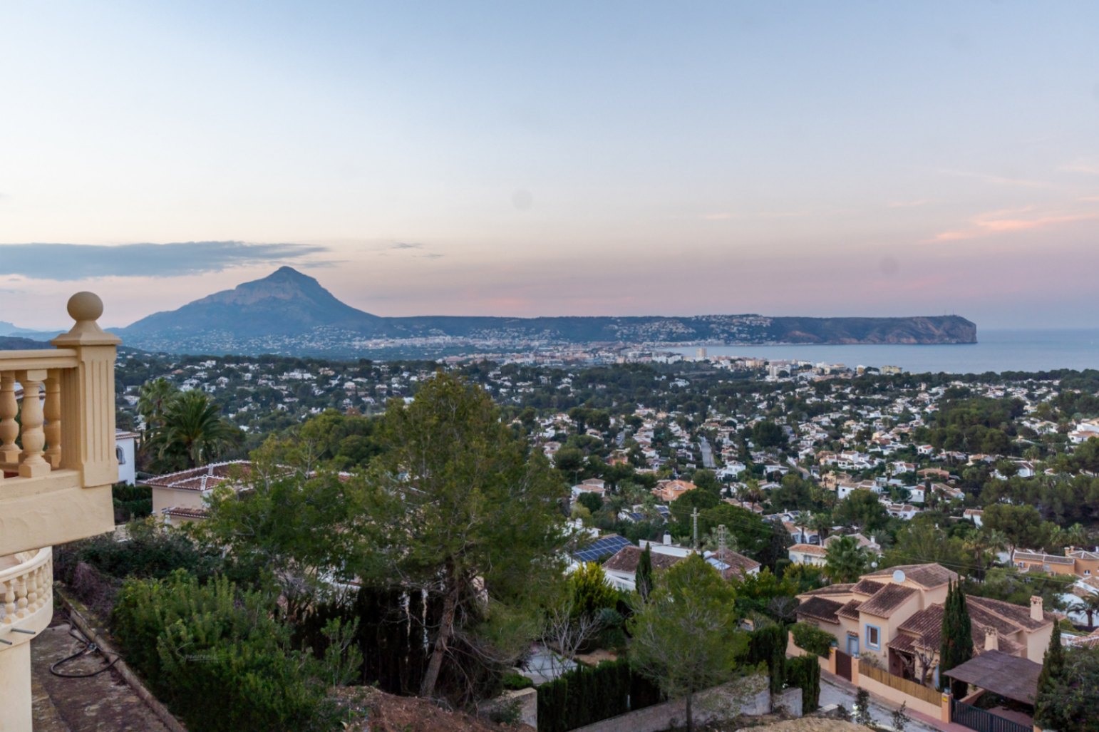 Panoramisch uitzicht vanaf het terras op de baai van Jávea, de Montgó-berg en Cabo San Antonio tijdens de schemering, omgeven door mediterrane tuinen.