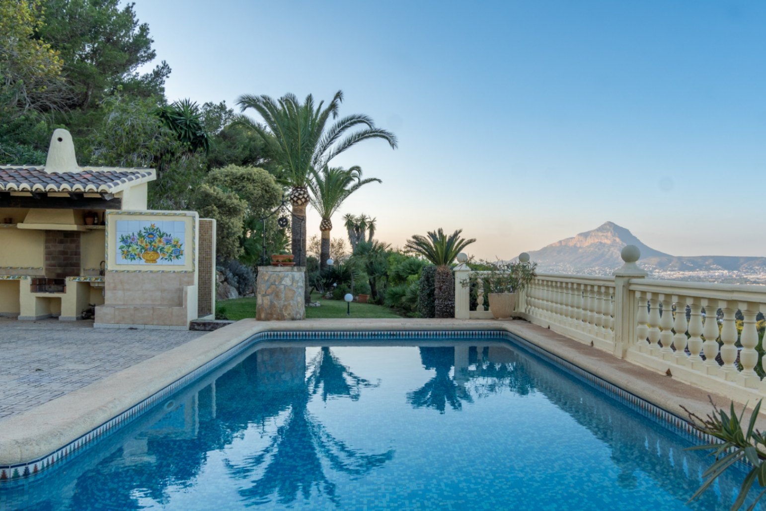 Rechthoekig mozaïekzwembad met overdekte buitenkeuken en keramisch tableau, gelegen in een mediterrane tuin met uitzicht op de Montgó.