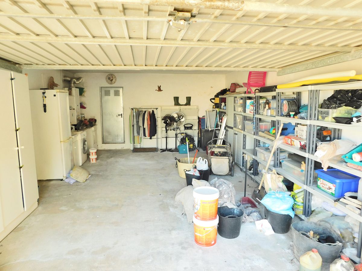 Ruime garage met betonvloer, metalen opbergrekken en een wasruimte uitgerust met een wasmachine en extra koelkast.