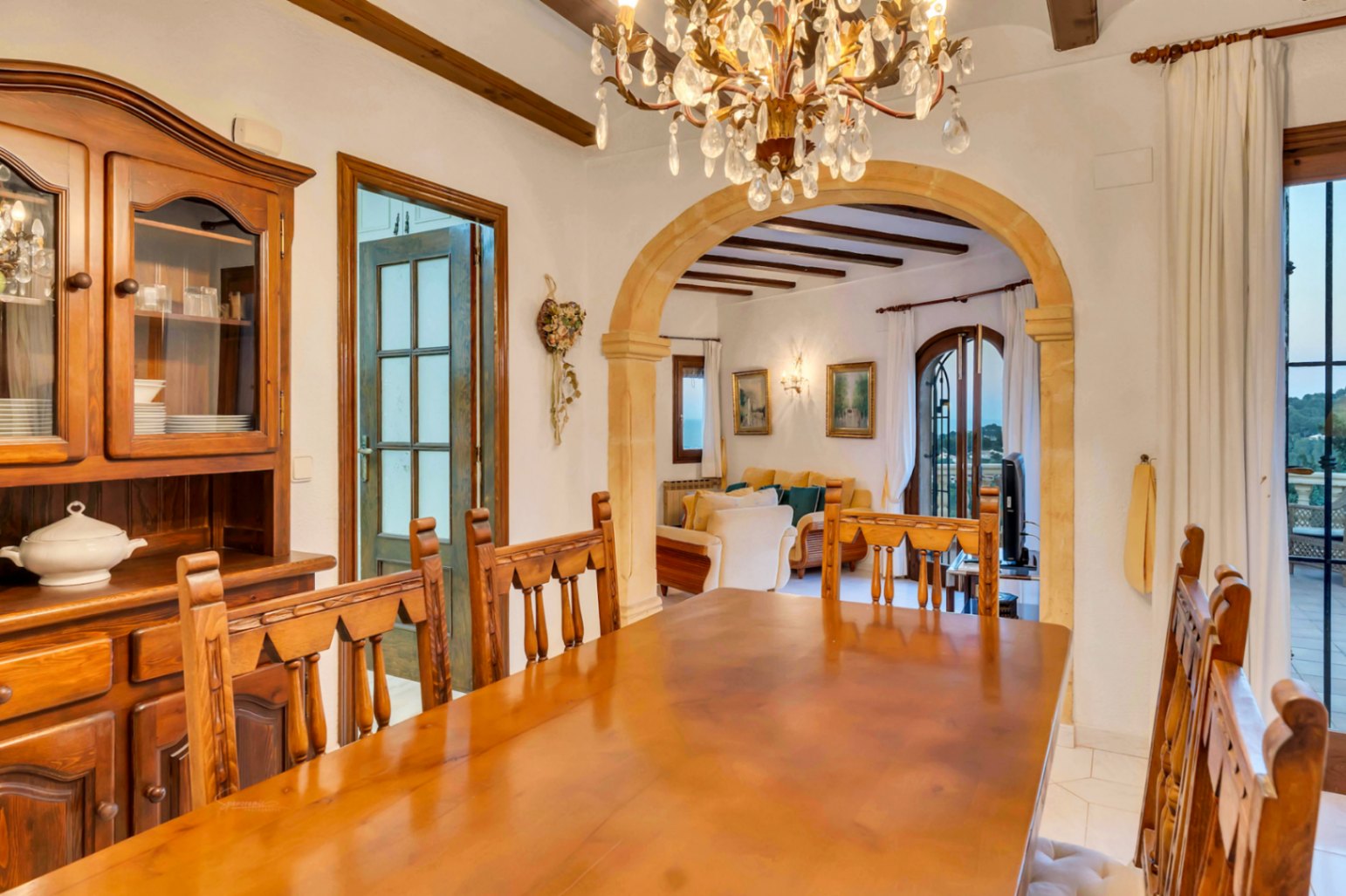Traditionele eetkamer met massief houten tafel, rustieke buffetkast en een boog van Tosca-natuursteen. Voorzien van houten plafondbalken en een kristallen kroonluchter.