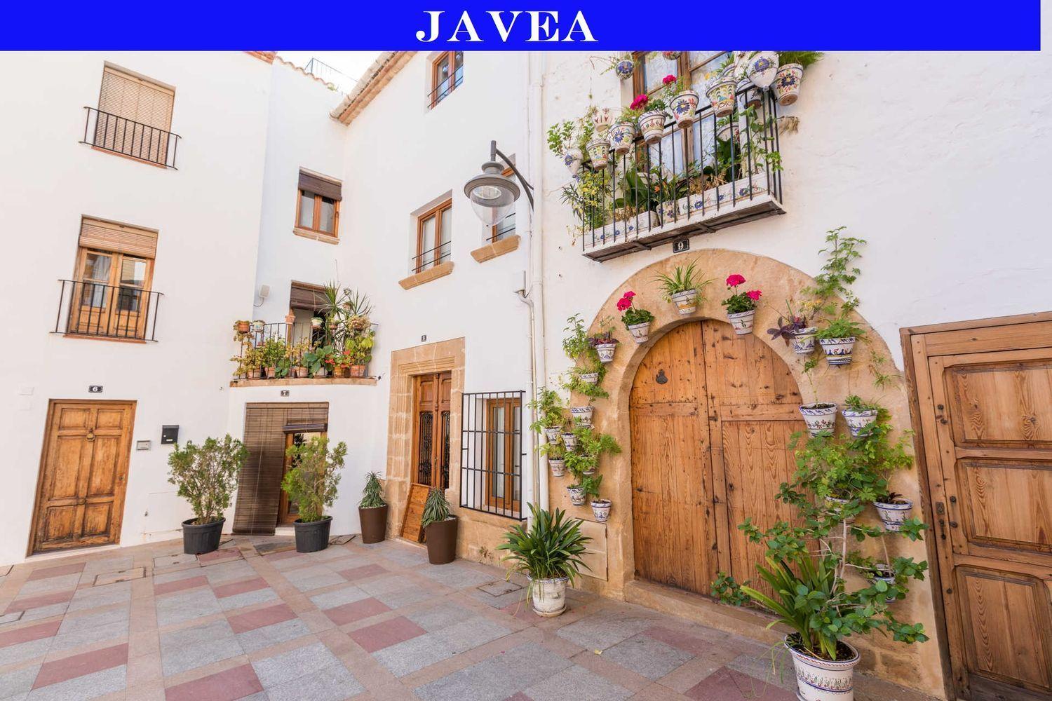 Traditionele gevel in het oude centrum van Jávea met houten deuren, tosca stenen bogen en decoratieve keramische bloempotten op witgekalkte muren.