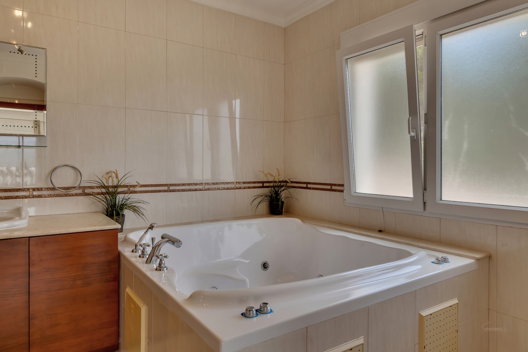 Badkamer met een ingebouwd hydromassagebad, crèmekleurige wandtegels met een decoratieve bies en een raam met matglas voor natuurlijk lichtinval.