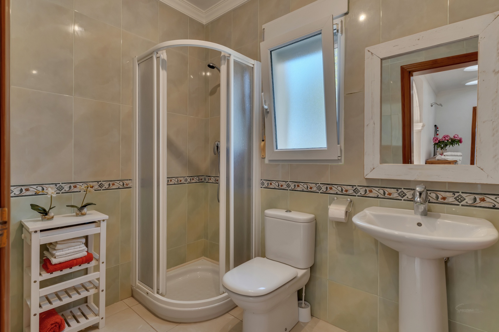 Badkamer voorzien van een halfronde hoekdouche, een kolomwastafel en betegelde wanden met een decoratieve sierstrip.