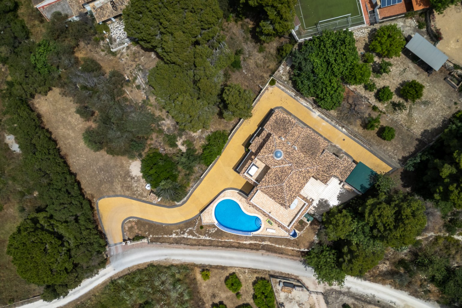 Bovenaanzicht van de villa met de indeling van het perceel, het pannendak met centrale koepel, de gebogen oprit en het zwembad.